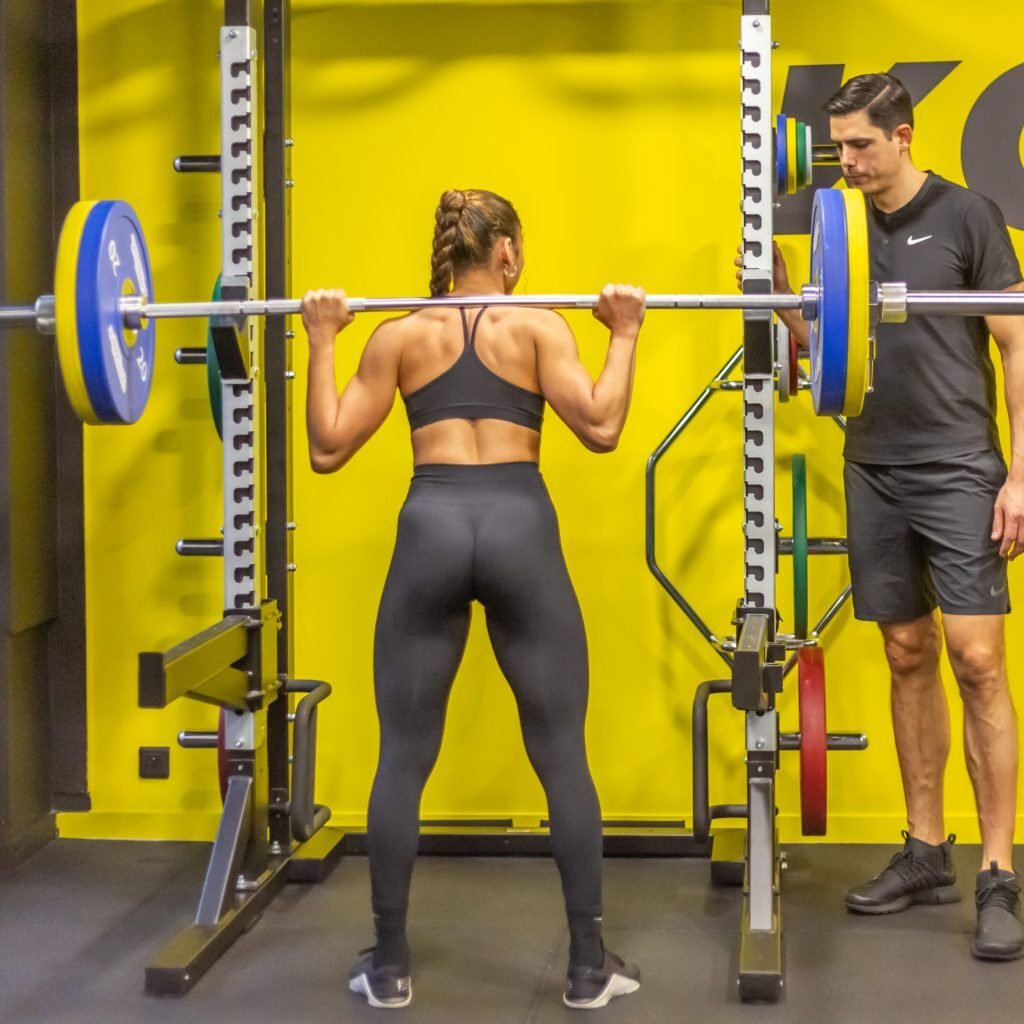 Exercice de renforcement avec barre encadr&eacute; par un kin&eacute;sith&eacute;rapeute du sport lors d&rsquo;une s&eacute;ance de r&eacute;&eacute;ducation