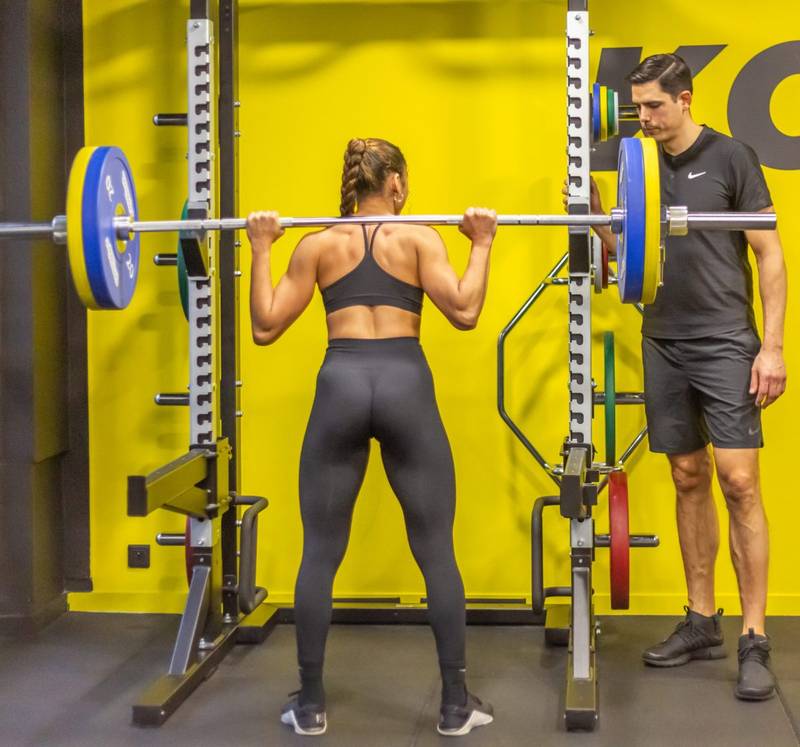 Exercice de renforcement avec barre encadr&eacute; par un kin&eacute;sith&eacute;rapeute du sport lors d&rsquo;une s&eacute;ance de r&eacute;&eacute;ducation